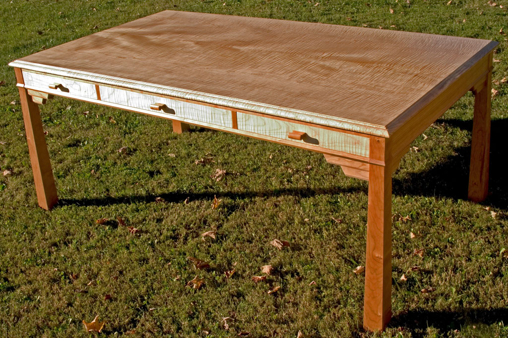 This curly maple and cherry map table features drawers and bracketed legs.